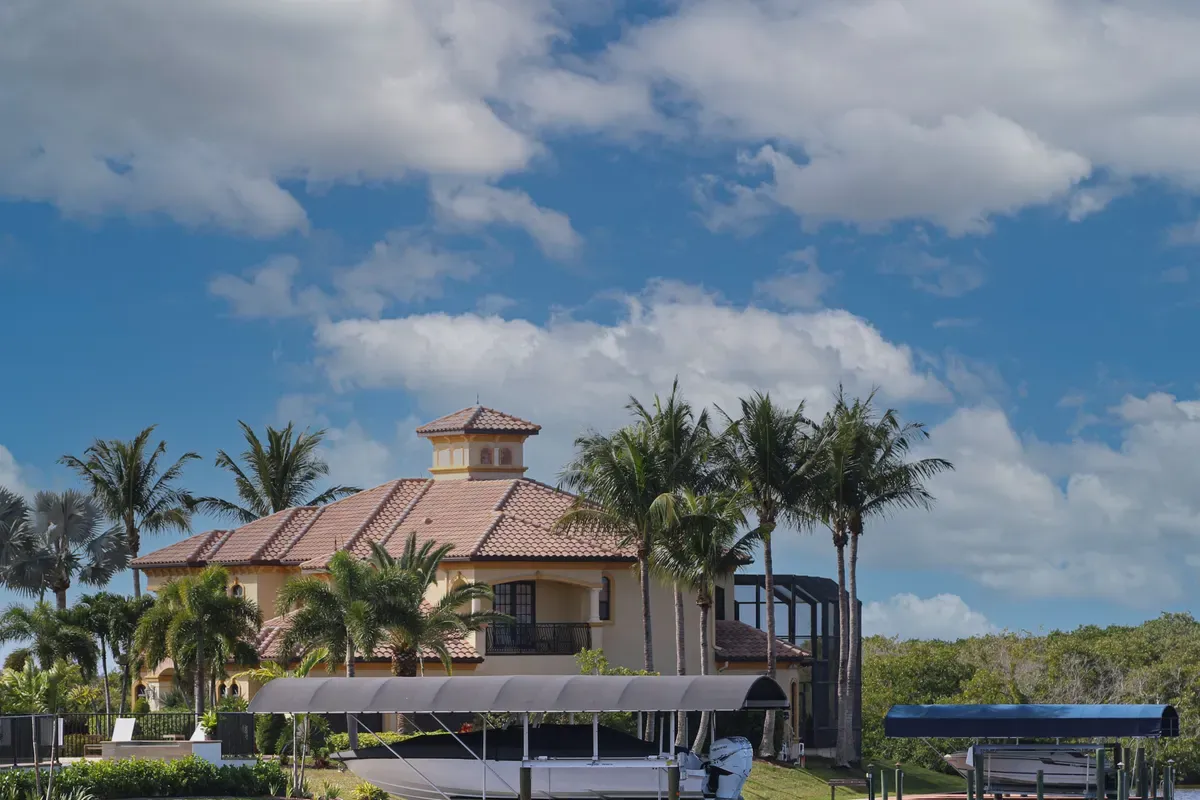 Tile-roofed waterfront home with palm trees and boat lifts under a bright blue sky, SummerGlen, Ocala
